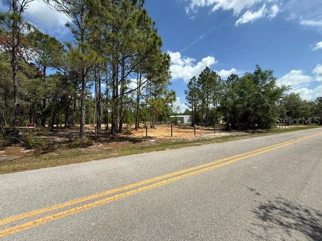 A vacant, partially cleared lot with trees sits alongside a paved road — 6123 OIL WELL ROAD, CLERMONT, FL