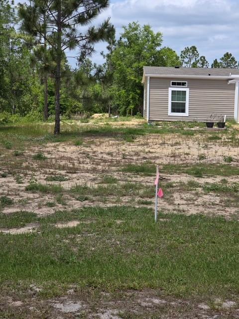 A view of a vacant, grassy lot next to the side of a tan house — 6123 OIL WELL ROAD, CLERMONT, FL