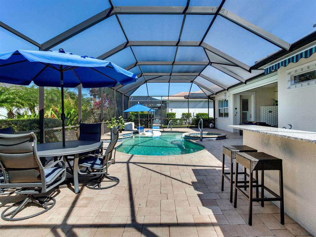A screened-in patio features a swimming pool, spa, dining set, and an outdoor bar — 5611 TIDEWATER PRESERVE BOULEVARD, BRADENTON, FL