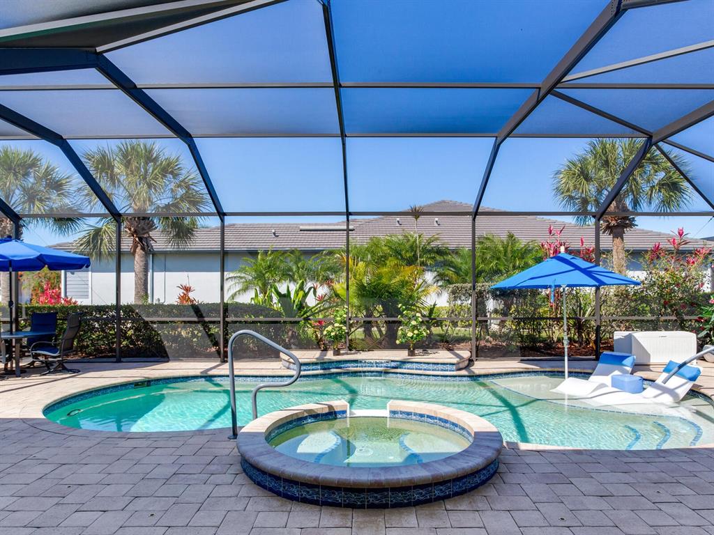 A screened-in pool area features a hot tub, lounge chairs, and blue umbrellas — 5611 TIDEWATER PRESERVE BOULEVARD, BRADENTON, FL