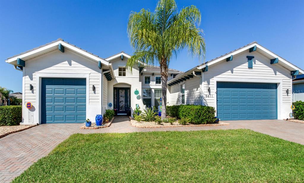 A single-story house with white siding, blue garage doors, and a central palm tree — 5611 TIDEWATER PRESERVE BOULEVARD, BRADENTON, FL