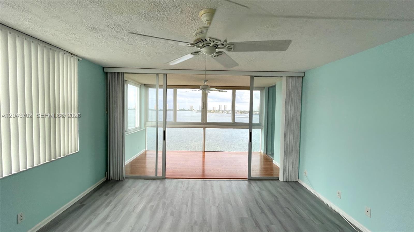 A living room with light blue walls, gray wood-look flooring, and a balcony overlooking water — 401 Lake Shore Dr # 801, Lake Park FL 33403, LAKE PARK, FL