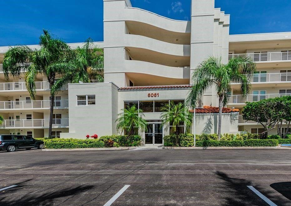 The exterior of a multi-story apartment building features a central entrance with palm trees — 6061 BAHIA DEL MAR CIRCLE UNIT 448, ST PETERSBURG, FL