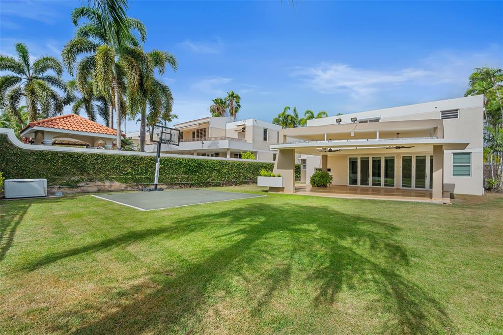 A backyard features a grassy lawn, a basketball hoop, and a covered patio area — 11 VIAJERA UNIT 76, GUAYNABO, PR