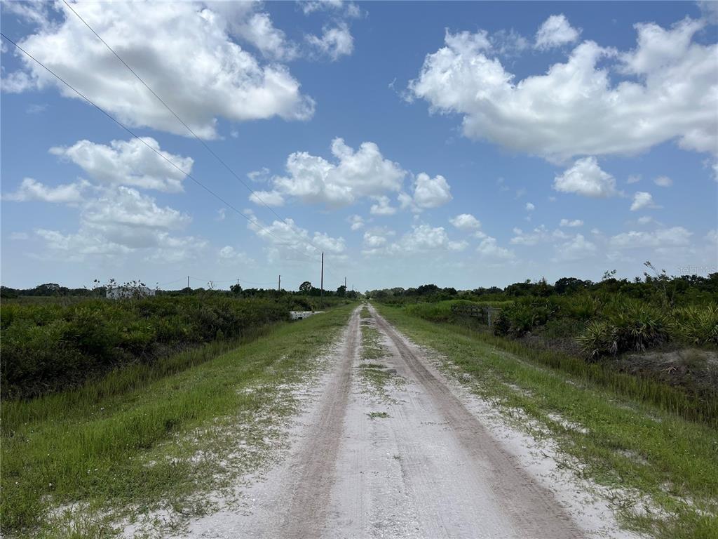 A dirt road stretches through a rural landscape under a bright, cloudy blue sky — 20106 NW 254TH STREET, OKEECHOBEE, FL