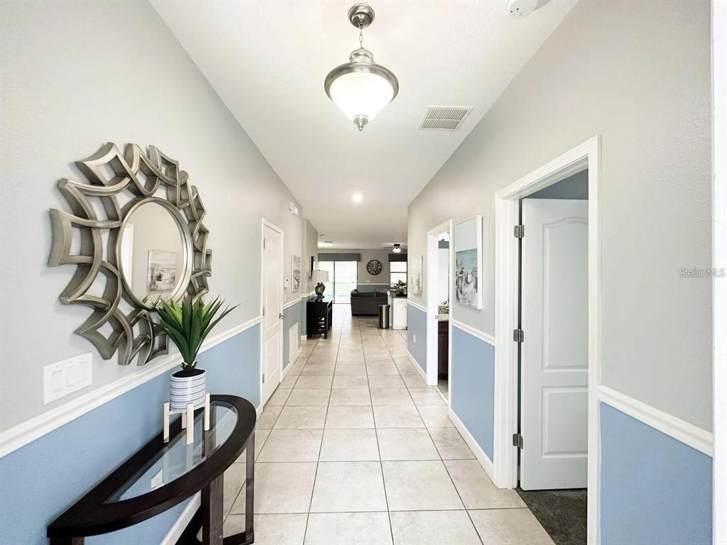 A hallway with light blue wainscoting, tile flooring, and a decorative mirror on the wall — 1469 ROLLING FARIWAY, DAVENPORT, FL
