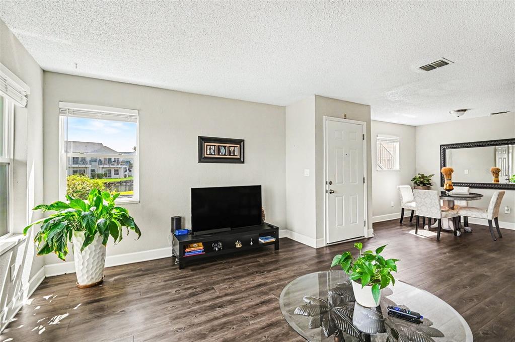 A living room with dark wood flooring, a television, and a dining area in back — 2552 WOODGATE BOULEVARD UNIT 107, ORLANDO, FL