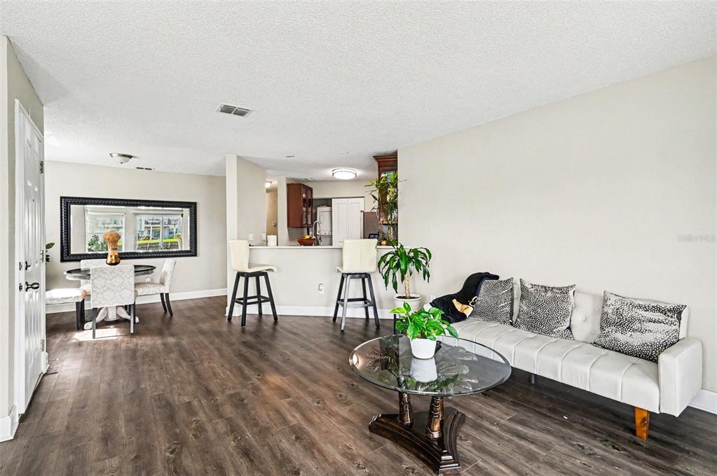 An open-concept living and dining area features wood-look flooring, a kitchen bar, and white walls — 2552 WOODGATE BOULEVARD UNIT 107, ORLANDO, FL