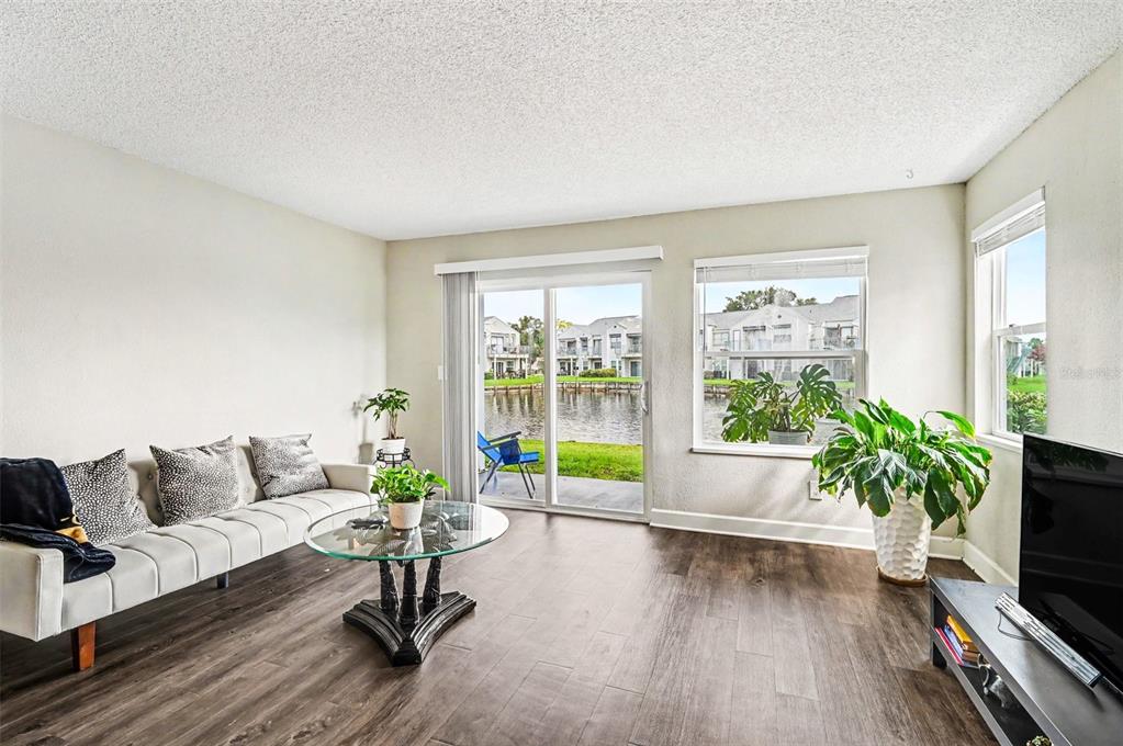 A living room with wood-look flooring, a sofa, a glass coffee table, and sliding glass doors — 2552 WOODGATE BOULEVARD UNIT 107, ORLANDO, FL