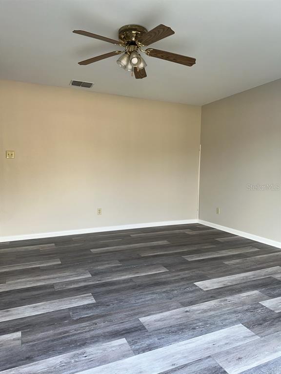 An empty room features gray wood-look plank flooring, beige walls, and a ceiling fan — 17608 SHADYSIDE CIRCLE, LUTZ, FL