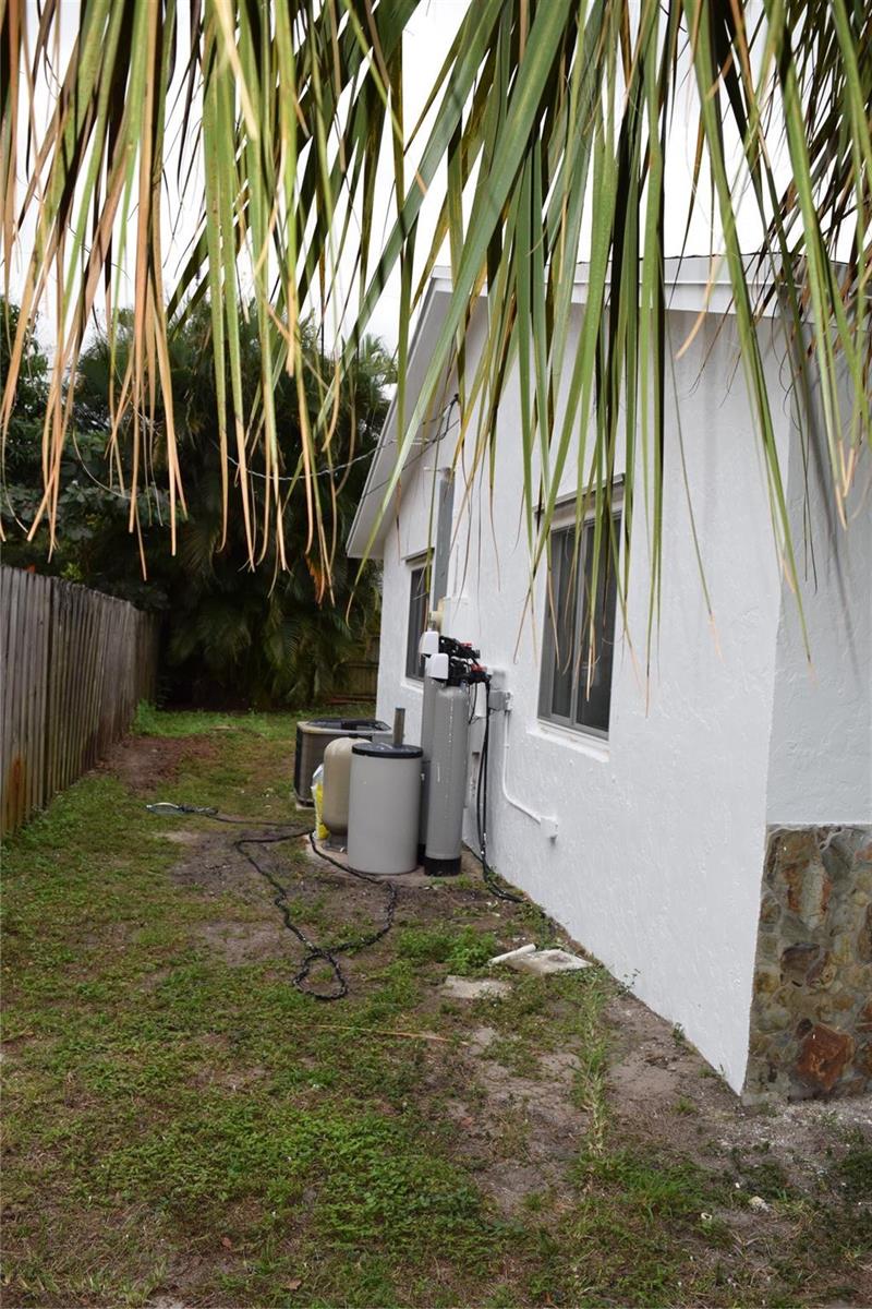 The exterior side of a white house features a water filtration system and HVAC unit — 3642 Harlowe Avenue, Boynton Beach FL 33436, BOYNTON BEACH, FL