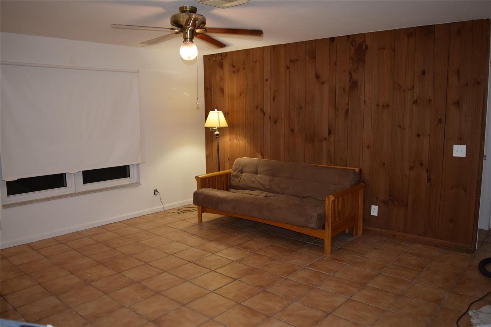 A room with tile flooring, a wood-paneled accent wall, a futon, and a ceiling fan — 3642 Harlowe Avenue, Boynton Beach FL 33436, BOYNTON BEACH, FL