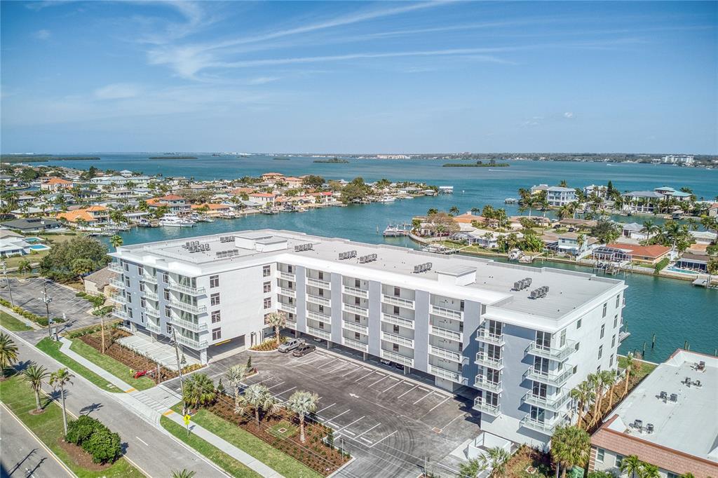An aerial view shows a multi-story apartment building with a parking lot near water — 415 ISLAND WAY UNIT 201, CLEARWATER BEACH, FL