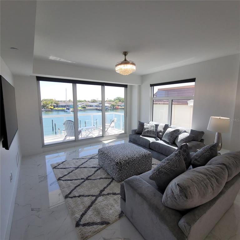 A modern living room features marble floors, grey furniture, and a balcony overlooking the water — 415 ISLAND WAY UNIT 201, CLEARWATER BEACH, FL