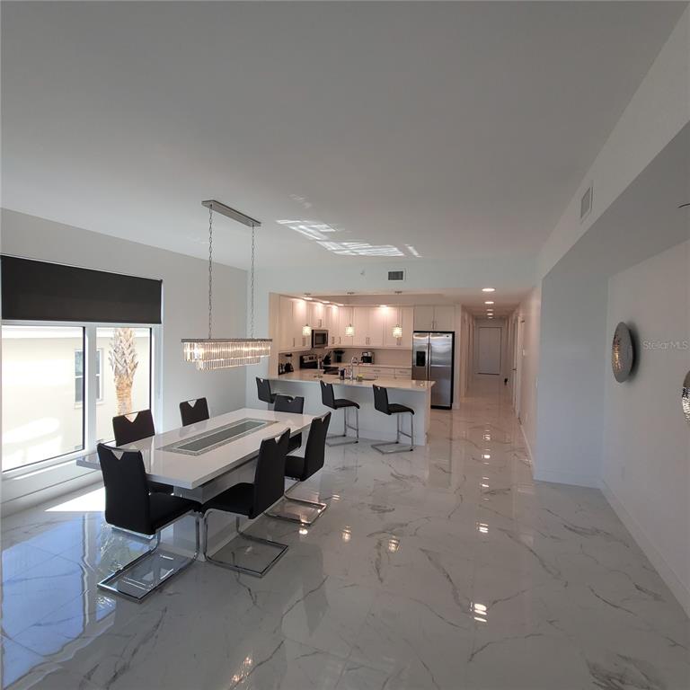 A dining area and kitchen feature white marble floors, modern furniture, and a crystal chandelier — 415 ISLAND WAY UNIT 201, CLEARWATER BEACH, FL