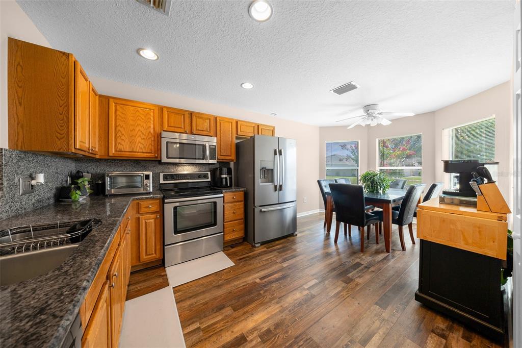 A kitchen with wood cabinets, stainless steel appliances, granite countertops, and an adjacent dining area — 15771 SW 13TH CIRCLE, OCALA, FL