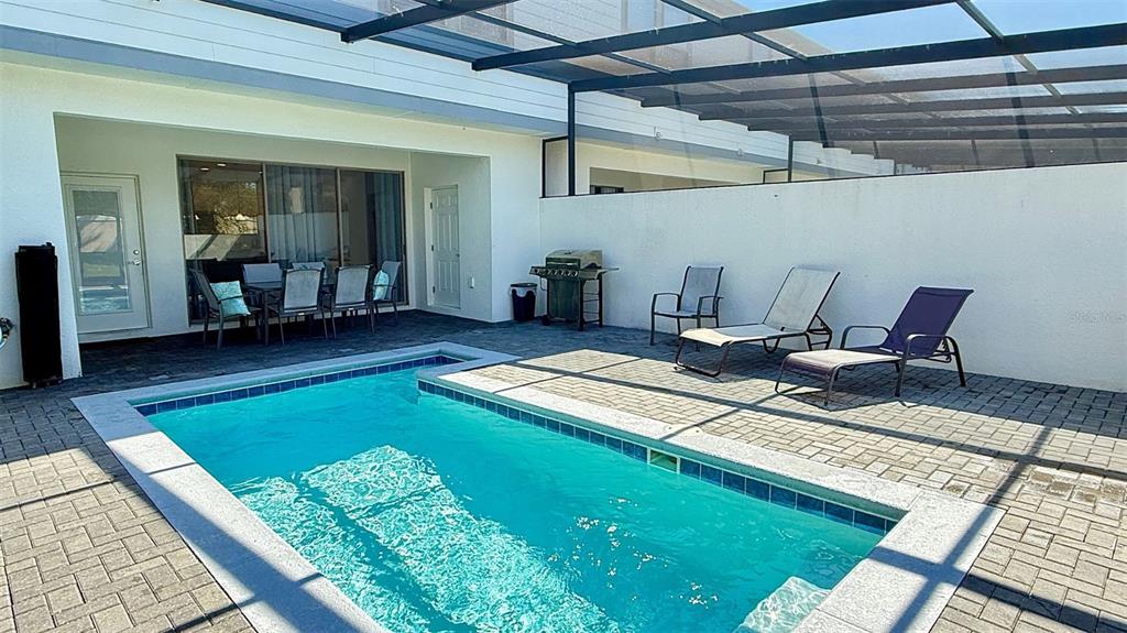 A backyard features a rectangular swimming pool, patio furniture, and a grill under a screen — 2414 DUBAI STREET, KISSIMMEE, FL