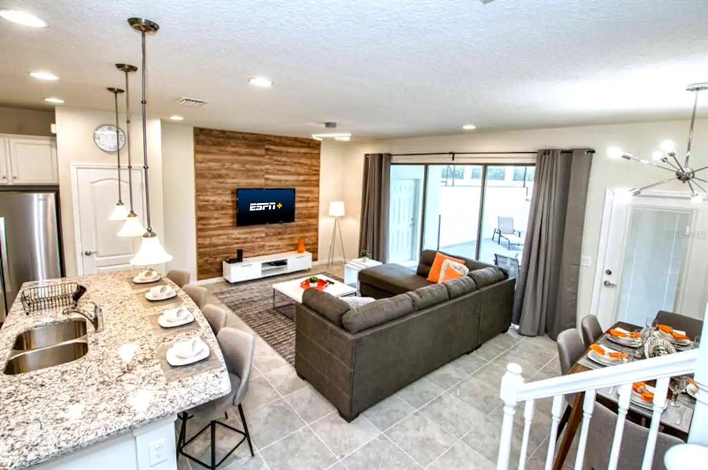 An open-concept living area features a kitchen island, wood-paneled accent wall, and gray sectional sofa — 2414 DUBAI STREET, KISSIMMEE, FL