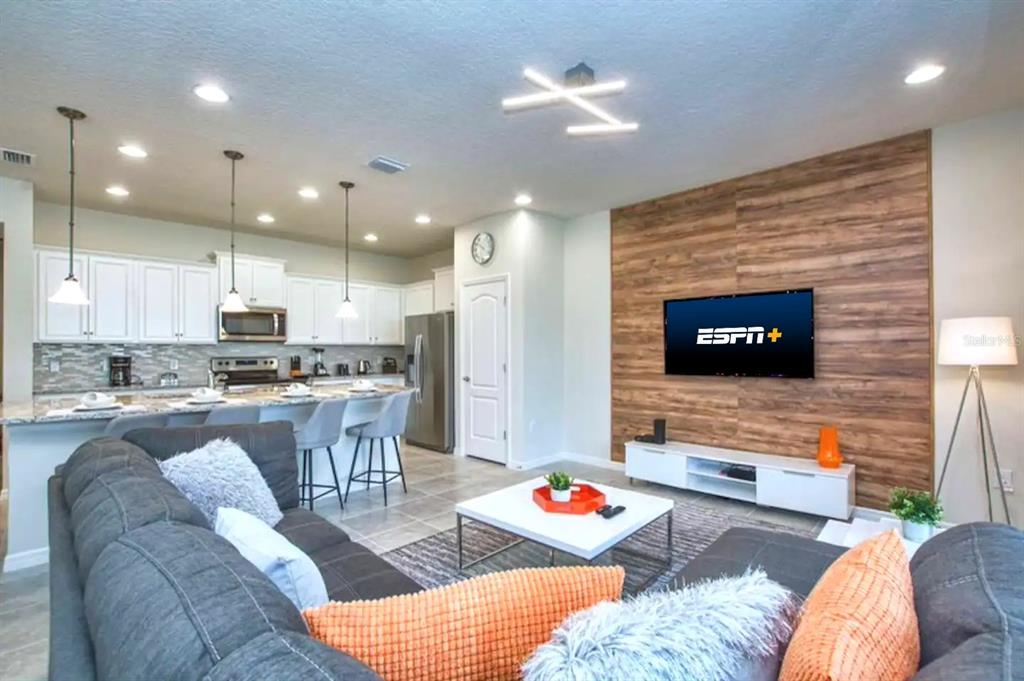 A living room features a wood-paneled accent wall, a gray sectional sofa, and an open kitchen — 2414 DUBAI STREET, KISSIMMEE, FL