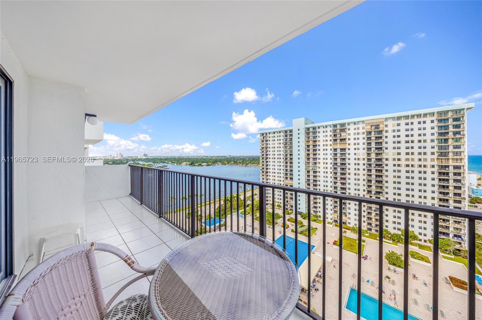 A balcony with a table and chairs overlooks a large apartment building and water — 1201 S Ocean Dr # 1903S, Hollywood FL 33019, HOLLYWOOD, FL