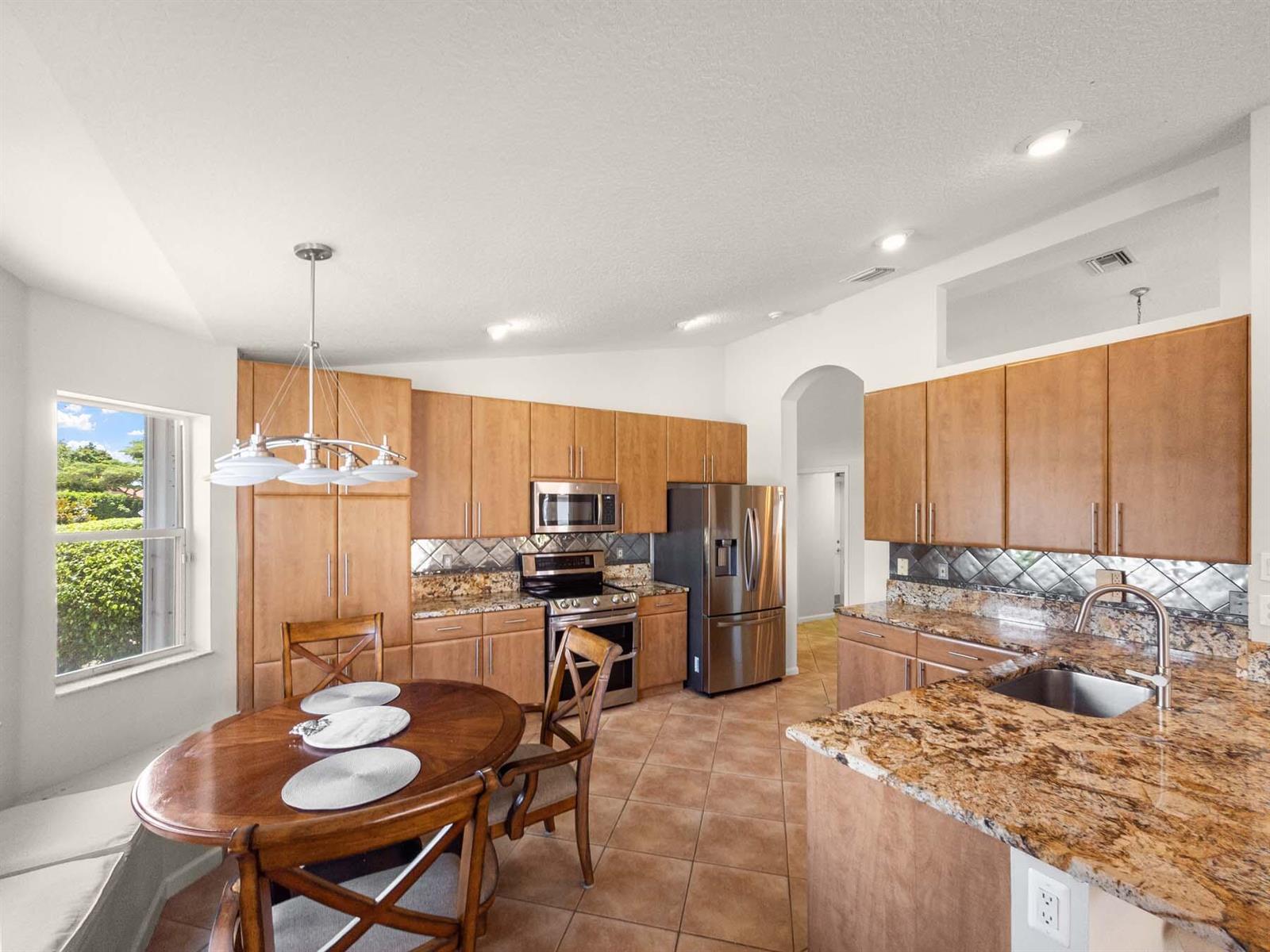 A kitchen features wood cabinets, granite countertops, stainless steel appliances, and a dining area — 5320 Glenville Drive, Boynton Beach FL 33437, BOYNTON BEACH, FL