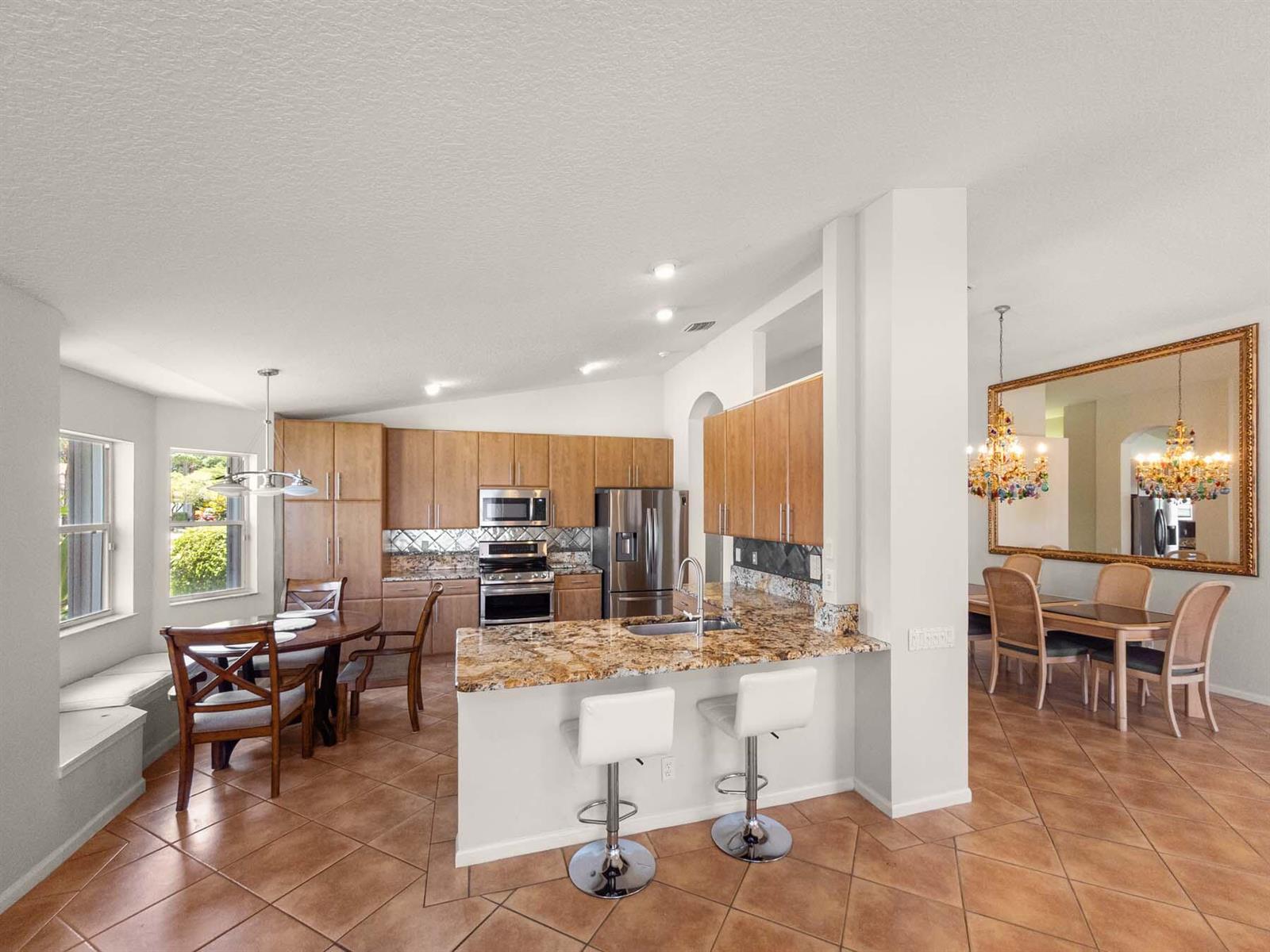 A kitchen with granite countertops, wood cabinets, and a breakfast bar overlooks a dining area — 5320 Glenville Drive, Boynton Beach FL 33437, BOYNTON BEACH, FL