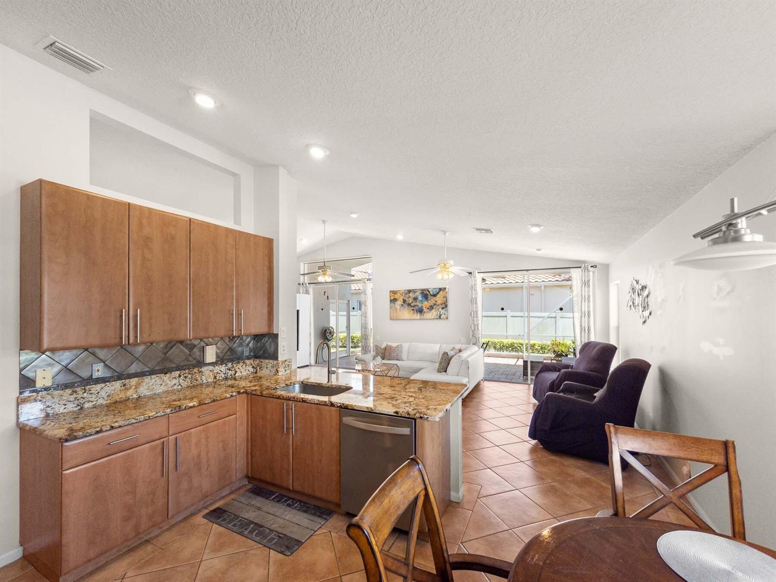 A kitchen with wood cabinets and granite countertops opens into a living area with tile — 5320 Glenville Drive, Boynton Beach FL 33437, BOYNTON BEACH, FL