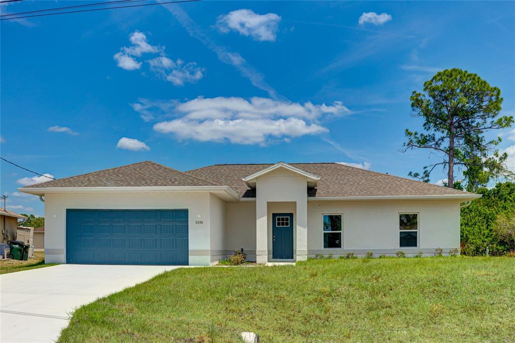 A single-story house with a blue garage door, a covered entryway, and a grassy lawn — 5330 IOTA COURT, NORTH PORT, FL