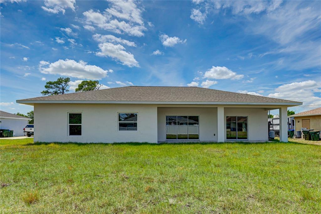 The rear exterior of a single-story house features a covered patio and a grassy yard — 5330 IOTA COURT, NORTH PORT, FL