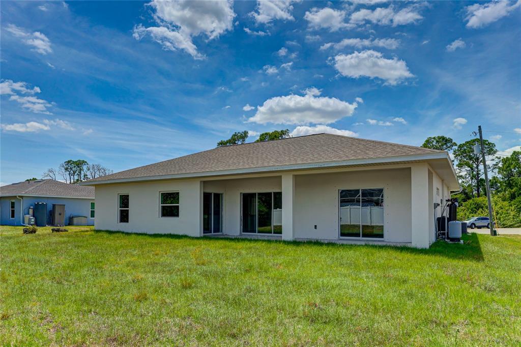 The rear exterior of a single-story house with a covered patio and a grassy yard — 5330 IOTA COURT, NORTH PORT, FL