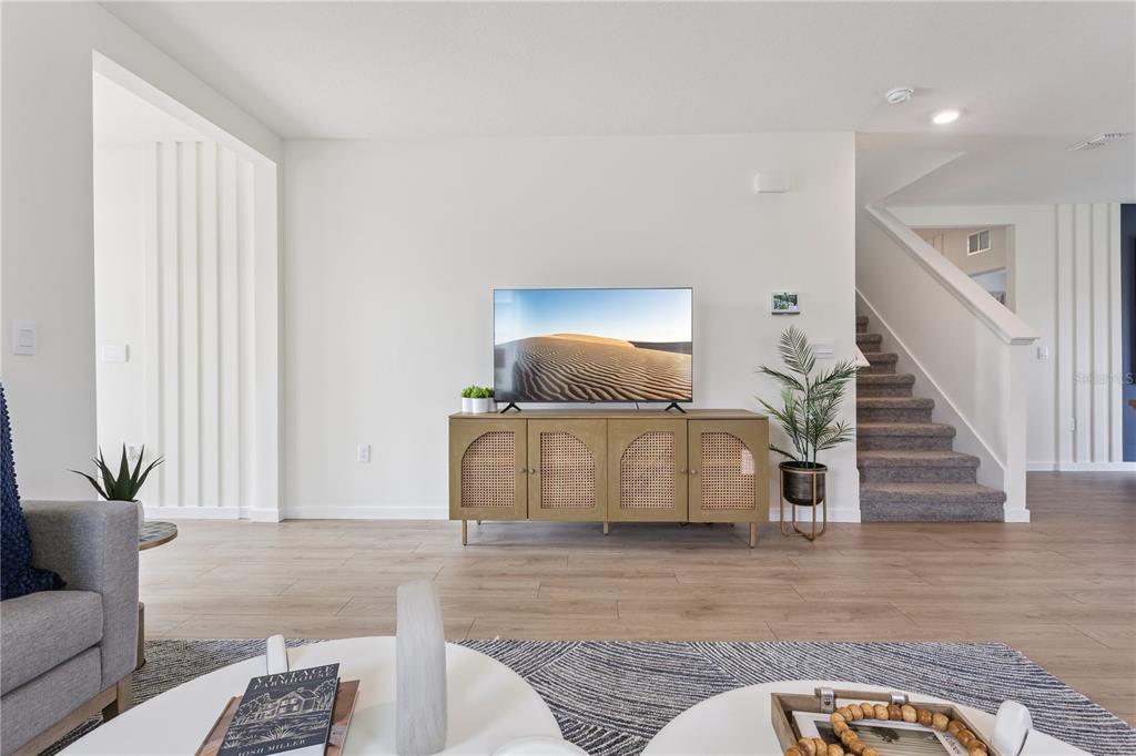 A living room features a television on a cane-front console, light wood flooring, and stairs — 5066 MARSHELDER STREET, APOPKA, FL