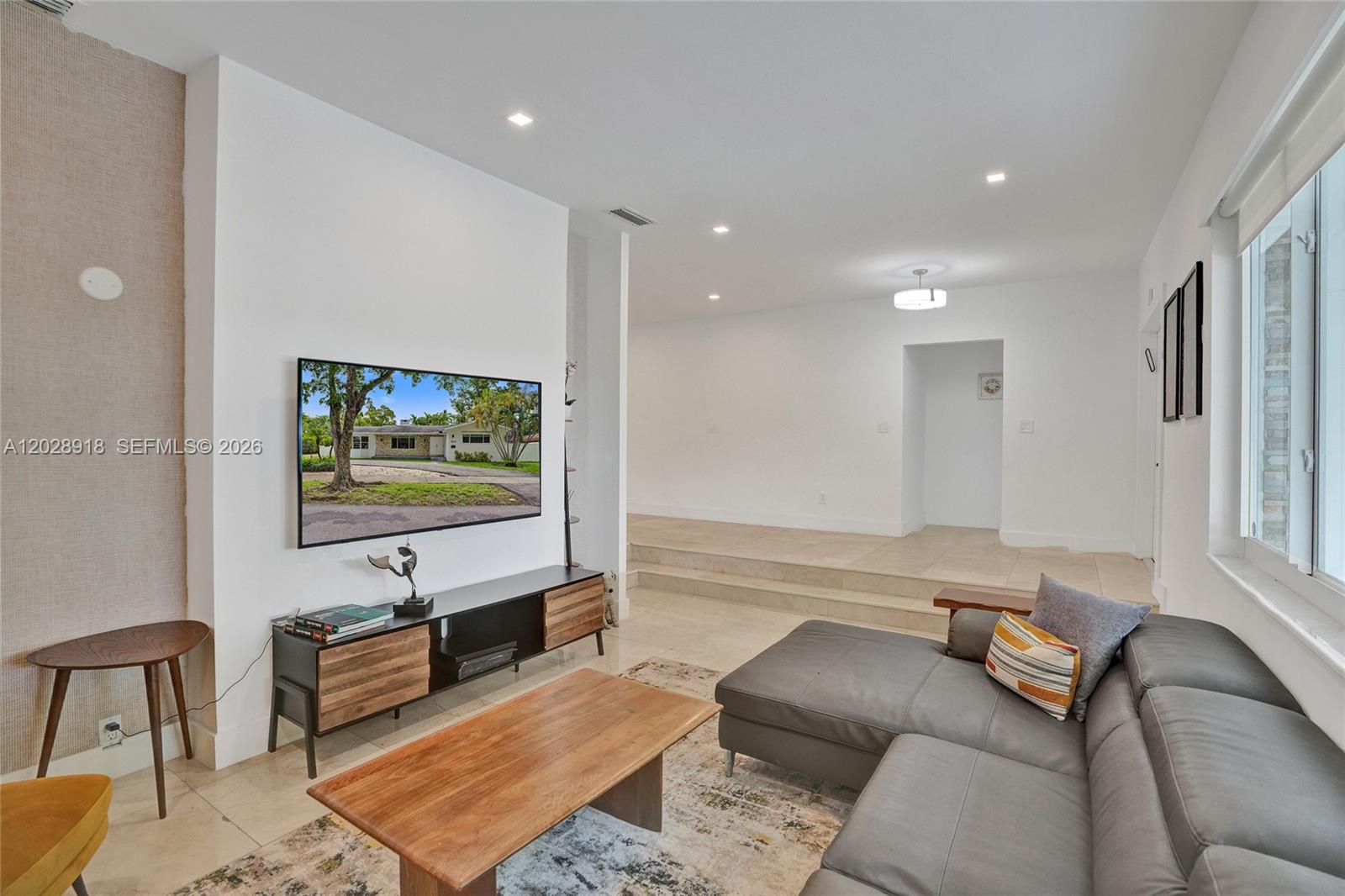 A living room features a wall-mounted television, a media console, and a gray sectional sofa — 18641 NE 21st Ave, Miami FL 33179, MIAMI, FL