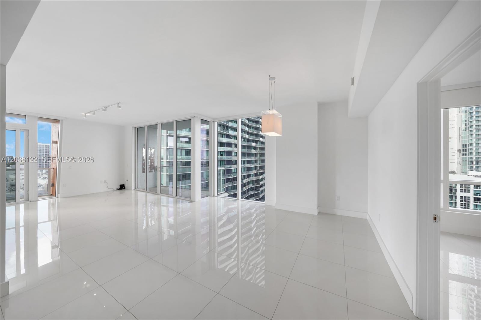 A bright, empty living area features white tile floors, floor-to-ceiling windows, and a modern pendant light — 601 NE 27th St # 1501, Miami FL 33137, MIAMI, FL