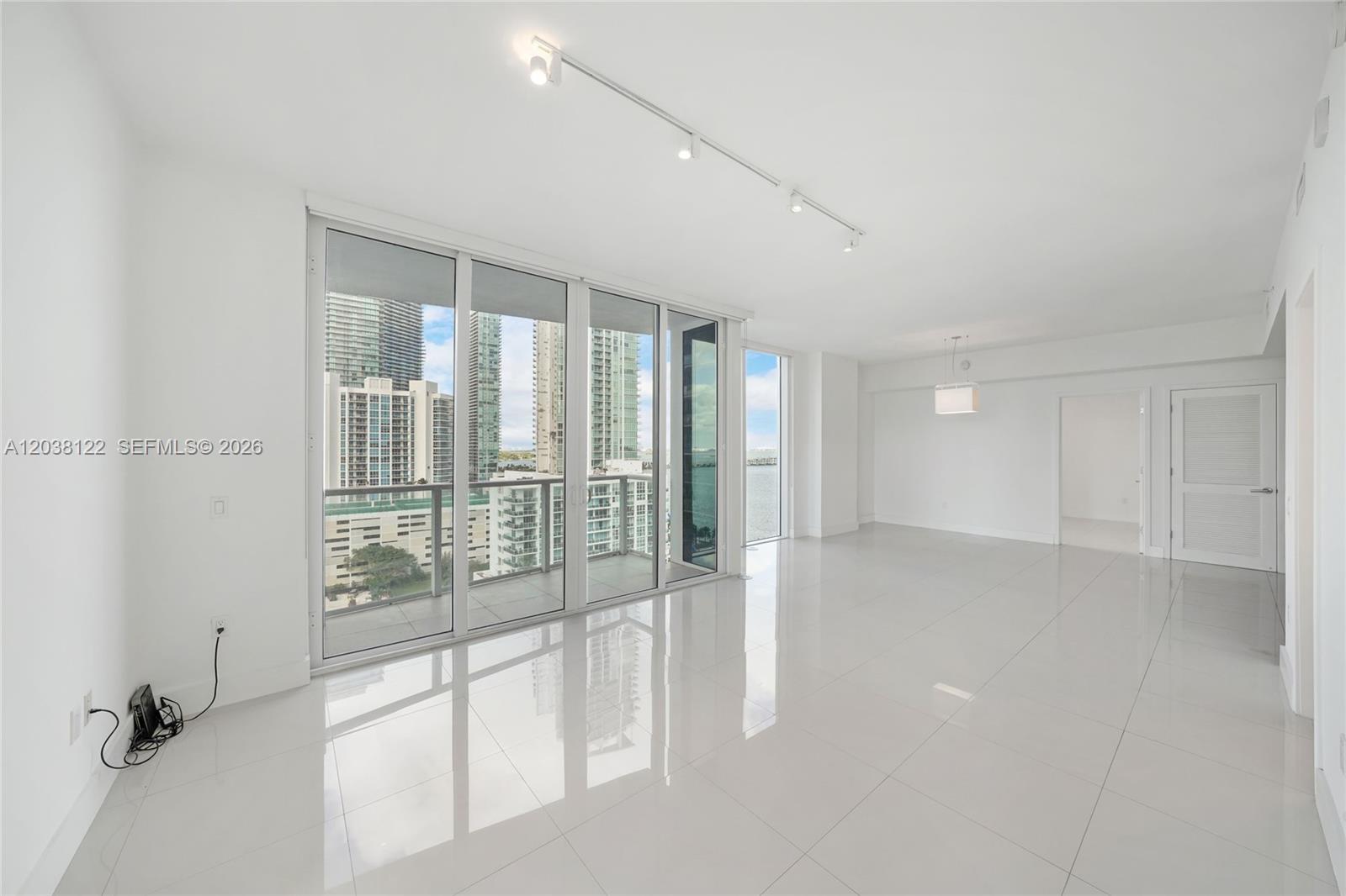 An empty room with white tile floors, track lighting, and floor-to-ceiling windows overlooking city buildings — 601 NE 27th St # 1501, Miami FL 33137, MIAMI, FL