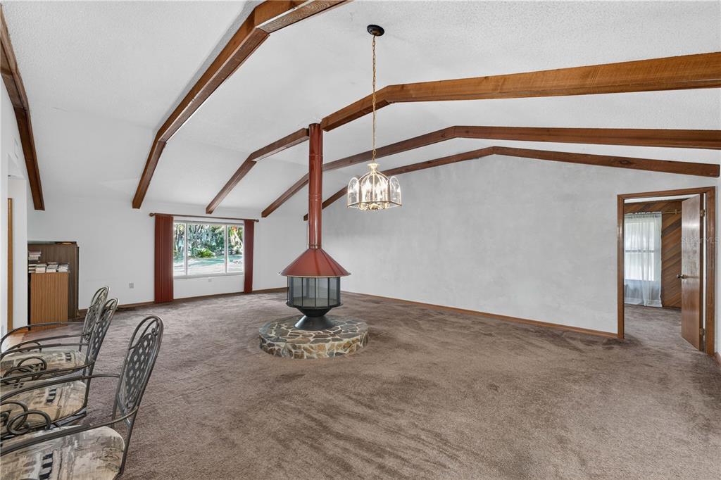 A living room features a vaulted ceiling with exposed beams, brown carpeting, and a central fireplace — 3385 WOODBERRY COURT, KISSIMMEE, FL