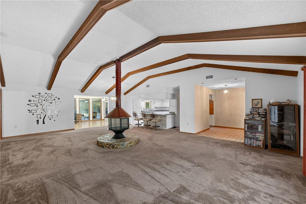 A spacious living room features a central fireplace, vaulted ceilings with wood beams, and carpet — 3385 WOODBERRY COURT, KISSIMMEE, FL