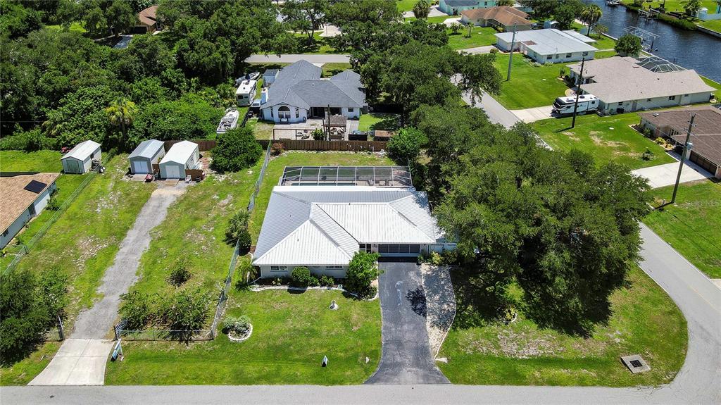 An aerial view shows a single-story house with a metal roof, pool enclosure, and driveway — 1175 BEAUMONT AVENUE, PORT CHARLOTTE, FL