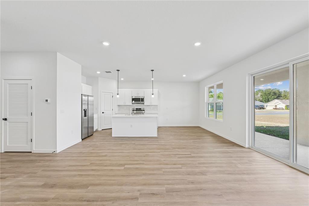 A bright, open-concept kitchen and living area features white cabinetry, stainless appliances, and wood-look flooring — 17875 SW 68TH PLACE, DUNNELLON, FL
