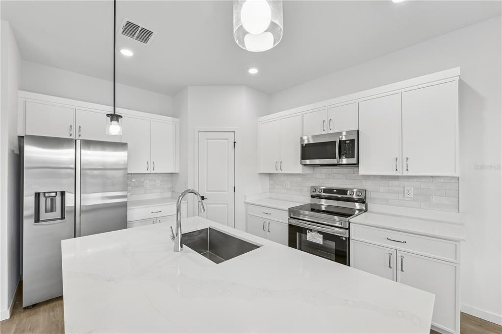 A modern kitchen features white cabinets, stainless steel appliances, and a large quartz-topped island — 17875 SW 68TH PLACE, DUNNELLON, FL