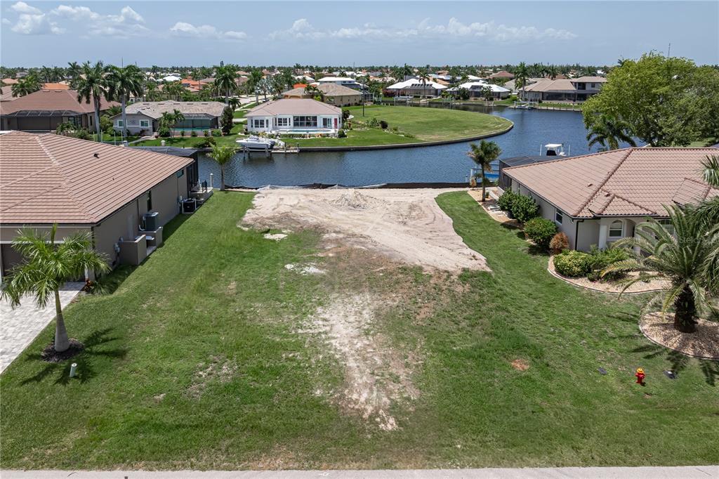An aerial view shows a vacant waterfront lot situated between two residential homes — 5143 ALMAR DRIVE, PUNTA GORDA, FL