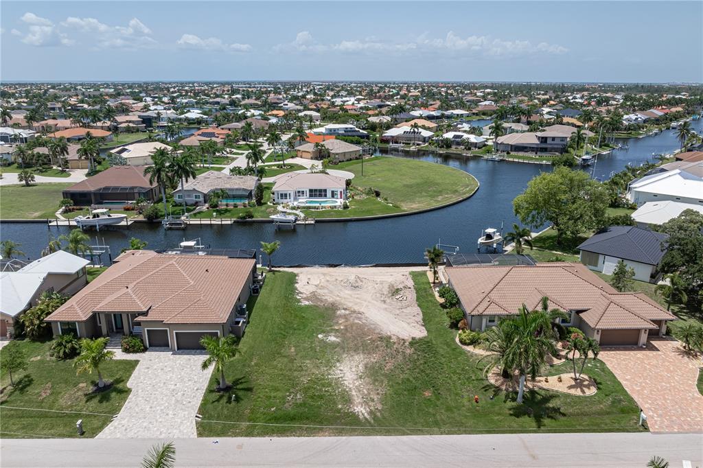 An aerial view shows a vacant waterfront lot situated between two single-family homes — 5143 ALMAR DRIVE, PUNTA GORDA, FL