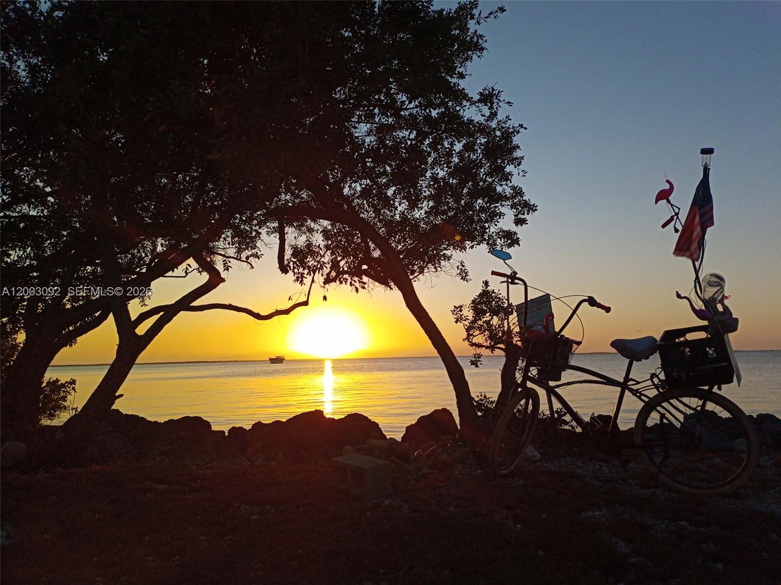 A bicycle with an American flag stands on a rocky shore during a sunset — 14 Bonita Ave, Key Largo FL 33037, KEY LARGO, FL