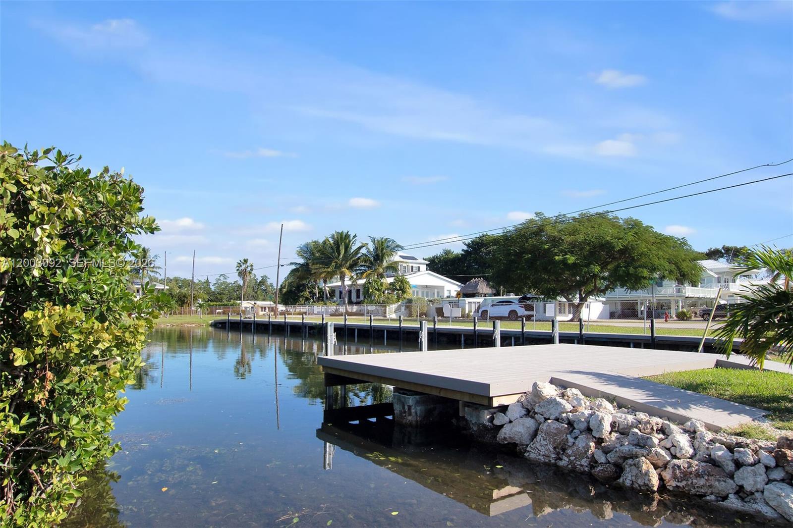 A wooden dock extends over a canal toward houses with palm trees under a blue sky — 14 Bonita Ave, Key Largo FL 33037, KEY LARGO, FL