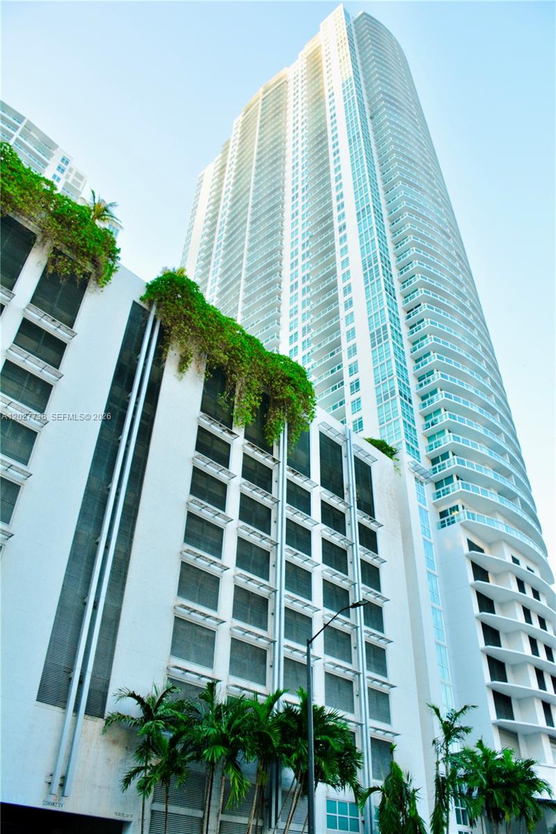 A tall residential skyscraper rises above a multi-level parking structure covered in hanging greenery — 951 BRICKELL # 2609, Miami FL 33131, MIAMI, FL