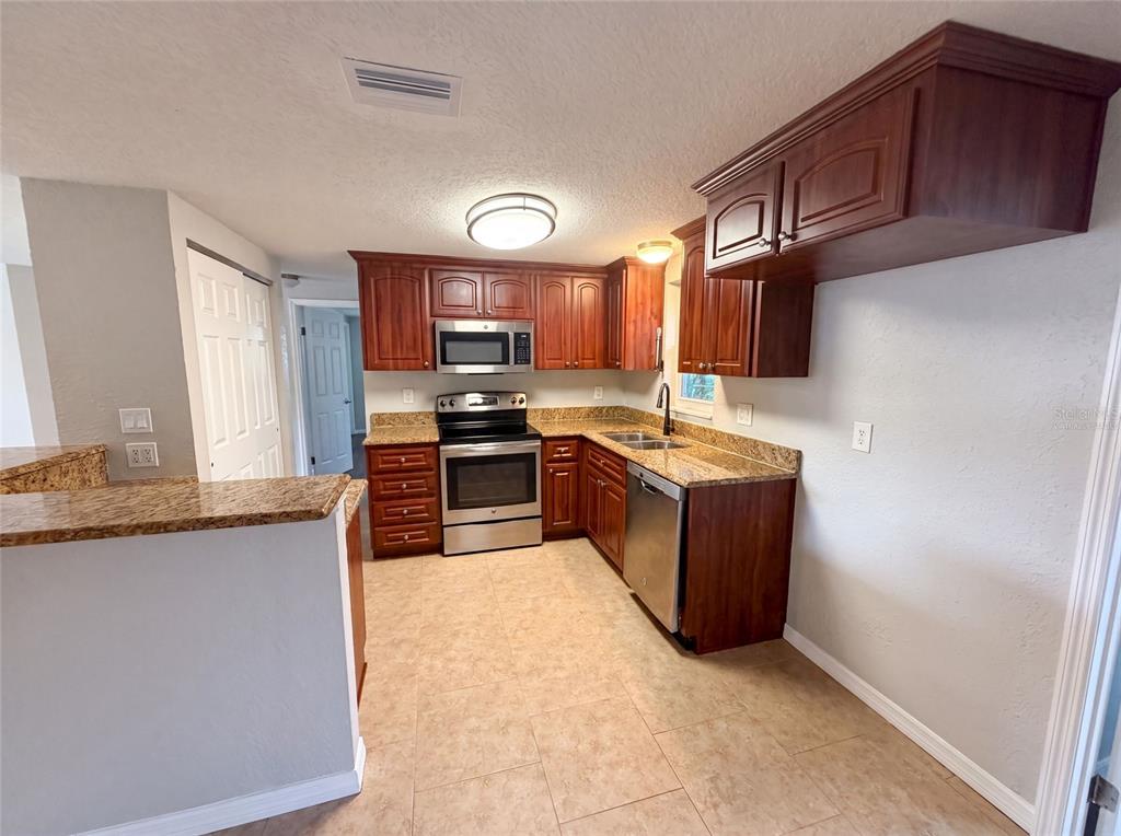 A kitchen features wood cabinets, granite countertops, stainless steel appliances, and tile flooring — 7037 GREEN STREET, NEW PORT RICHEY, FL