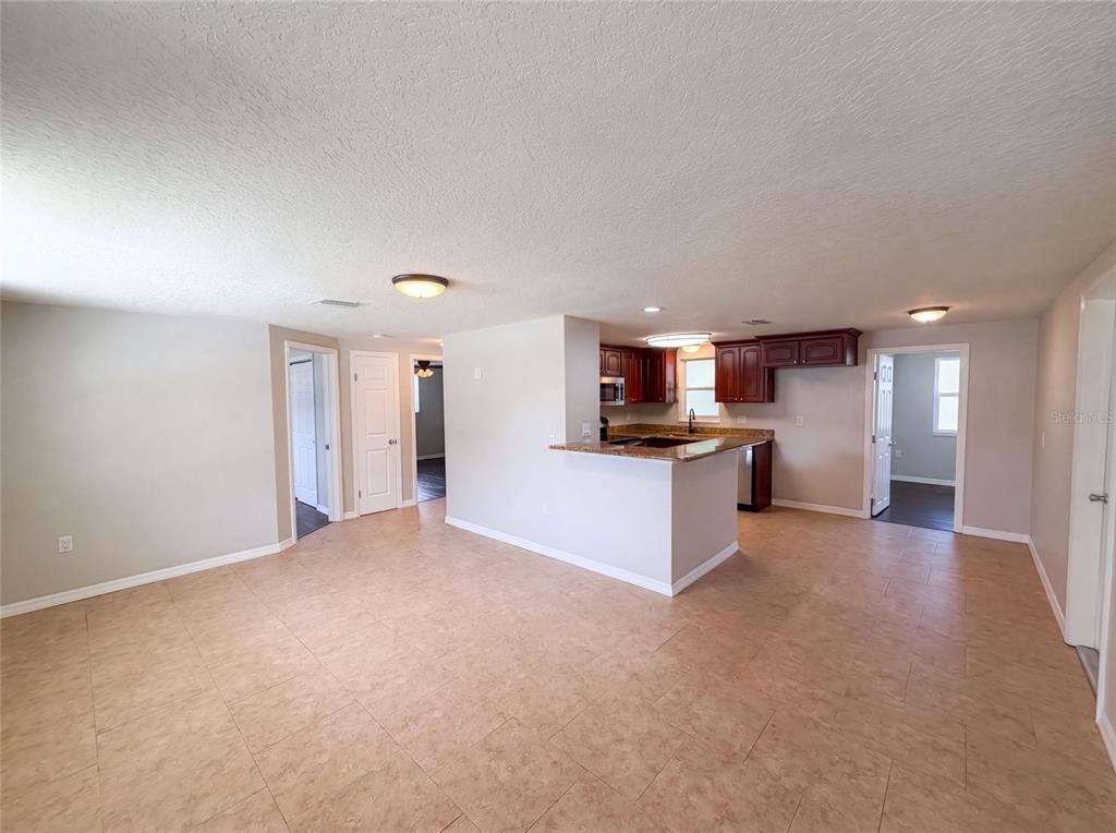 An open-concept living area features light tile flooring, a kitchen peninsula, and dark wood cabinetry — 7037 GREEN STREET, NEW PORT RICHEY, FL