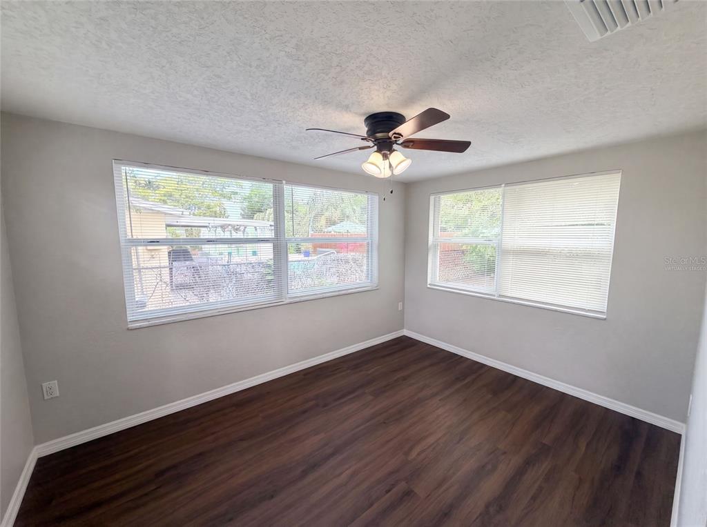 An empty room features dark wood-look flooring, light gray walls, and a ceiling fan — 7037 GREEN STREET, NEW PORT RICHEY, FL