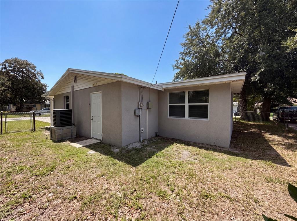 The exterior of a single-story house features a white door, a window, and an AC unit — 7037 GREEN STREET, NEW PORT RICHEY, FL