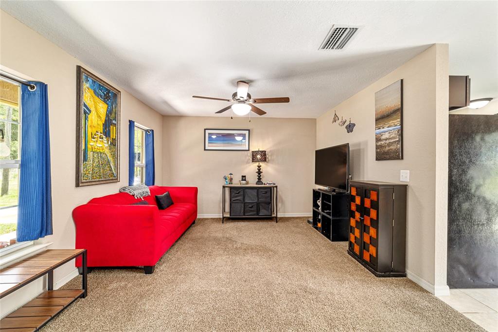 A living room features a red sofa, beige walls, carpeted flooring, and a ceiling fan — 2854 SE 140TH LANE, SUMMERFIELD, FL