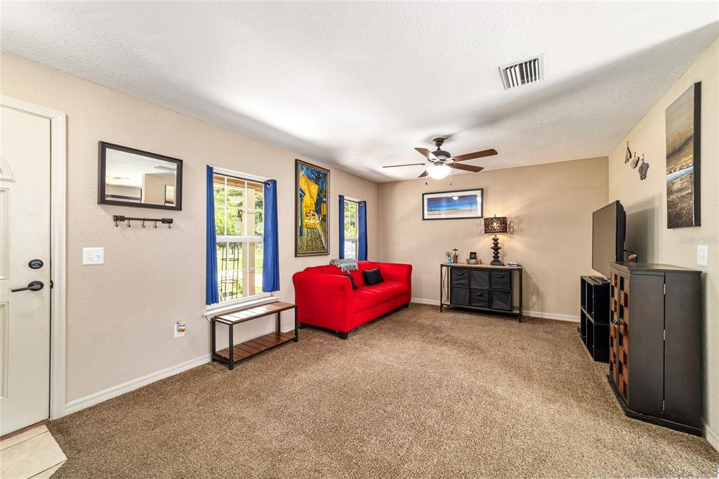 A living room with beige walls, brown carpet, a red sofa, and a television — 2854 SE 140TH LANE, SUMMERFIELD, FL